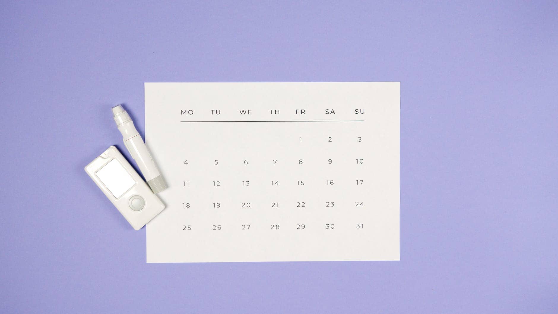 a glucometer and a lancet pen beside a calendar